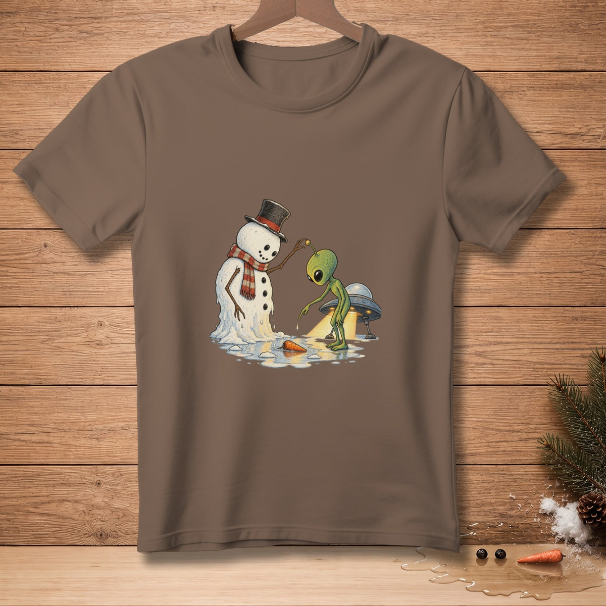 Brown t-shirt with melting snowman, alien, and UFO graphic on wooden background.