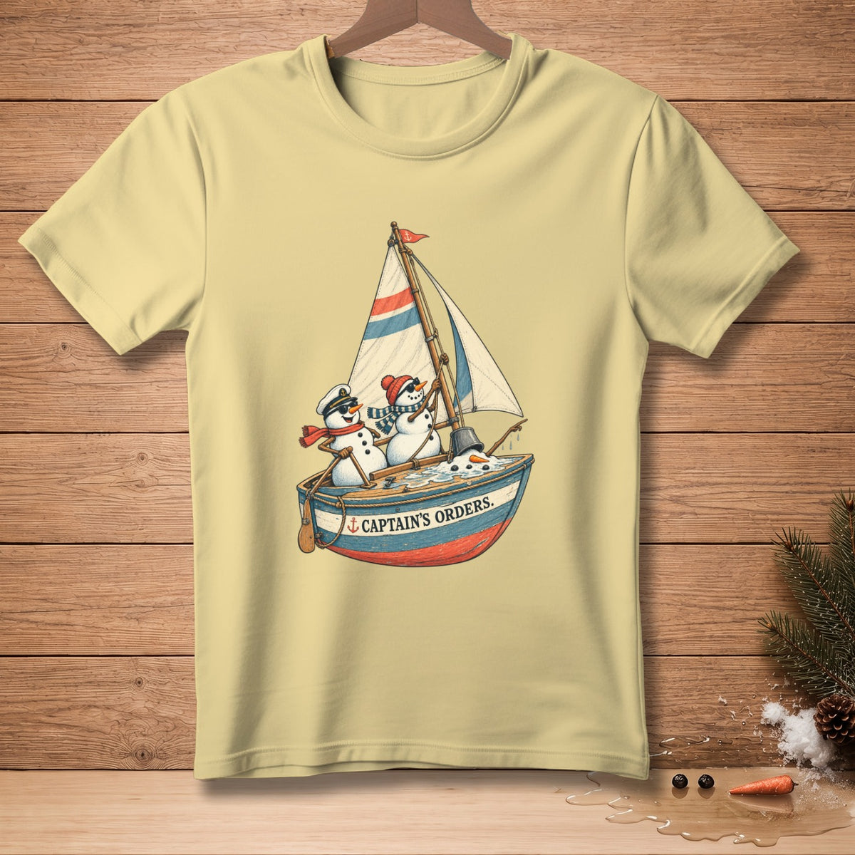 Light yellow t-shirt with a sailboat graphic featuring three snowmen and the text "CAPTAIN'S ORDERS."