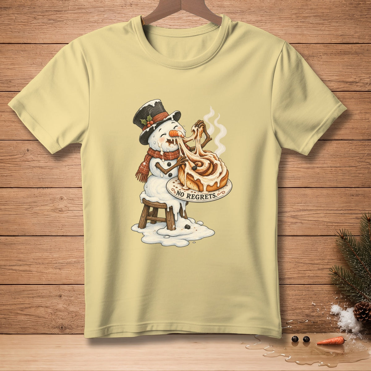 Light yellow t-shirt with snowman melting while eating cinnamon roll, saying "No Regrets".