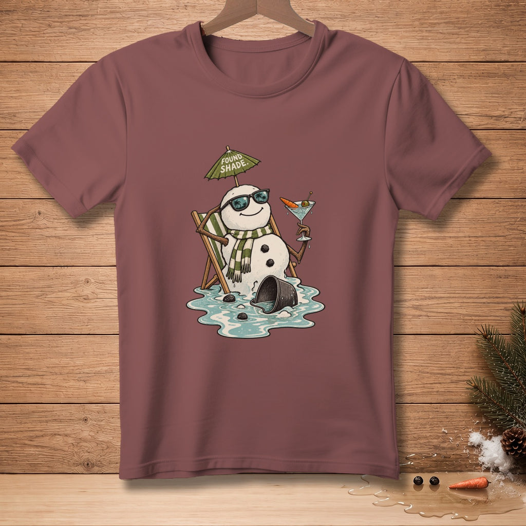 Melting snowman in beach chair with umbrella that reads "FOUND SHADE," holding a martini.