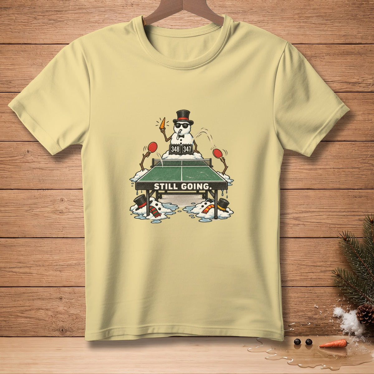 T-shirt with snowmen playing ping pong and "STILL GOING." text.