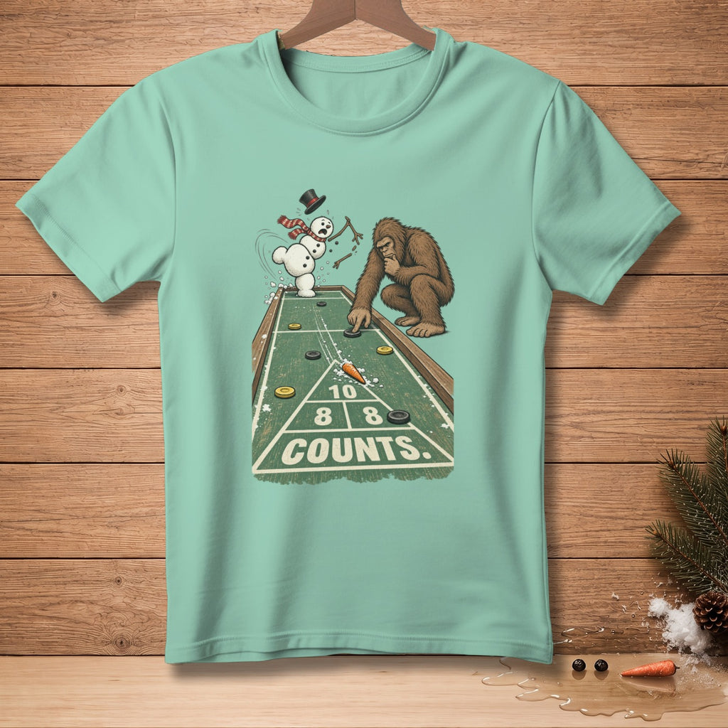 Bigfoot and snowman play shuffleboard on t-shirt graphic with "COUNTS" text.