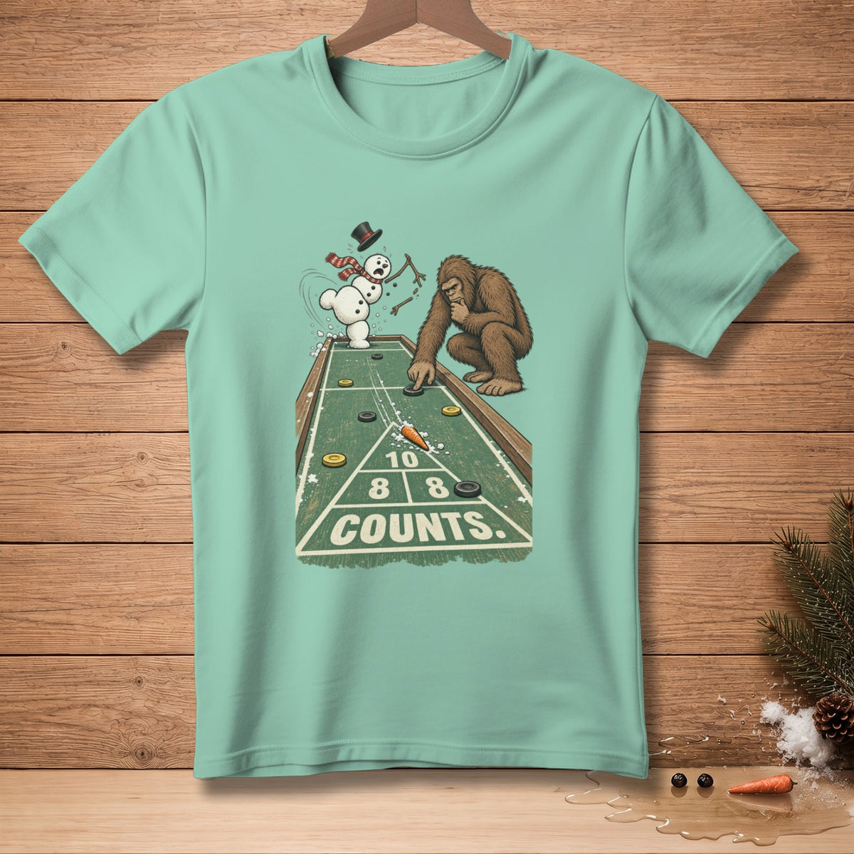 Bigfoot and snowman play shuffleboard on t-shirt graphic with "COUNTS" text.