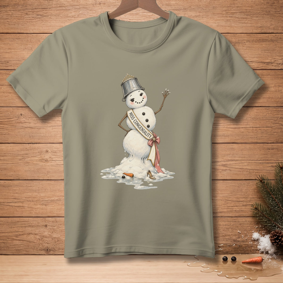 Melting snowman wearing a bucket crown and "Miss Congeniality" sash on a grey t-shirt.