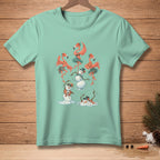Mint green t-shirt featuring dancing flamingos and melting snowmen with Hawaiian leis and hats.
