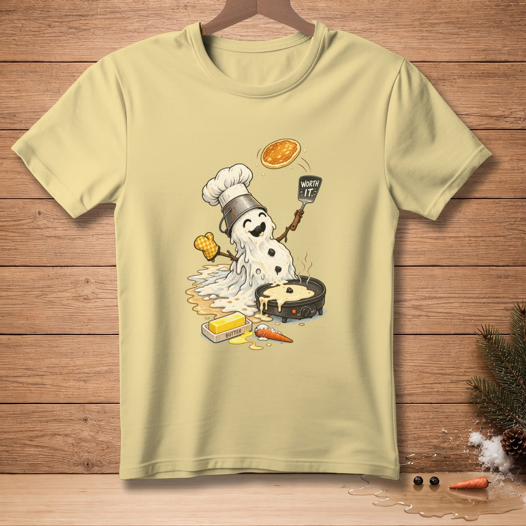 Melting snowman chef flips a pancake with "Worth It" spatula on a light yellow t-shirt.