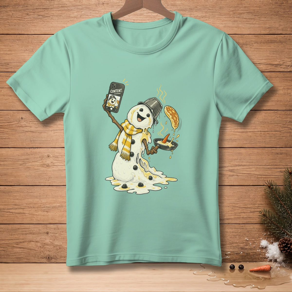 Melting snowman holding phone with "CONTENT" and cooking pancakes on a teal t-shirt.