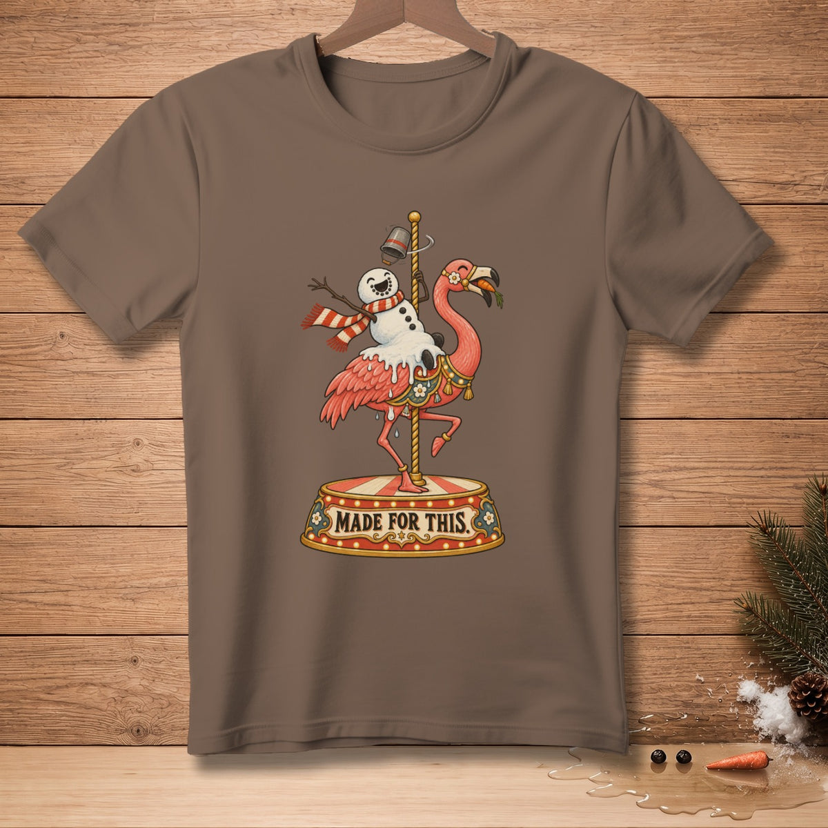 Brown t-shirt with a flamingo riding a carousel pole, holding a snowman and wearing a scarf.