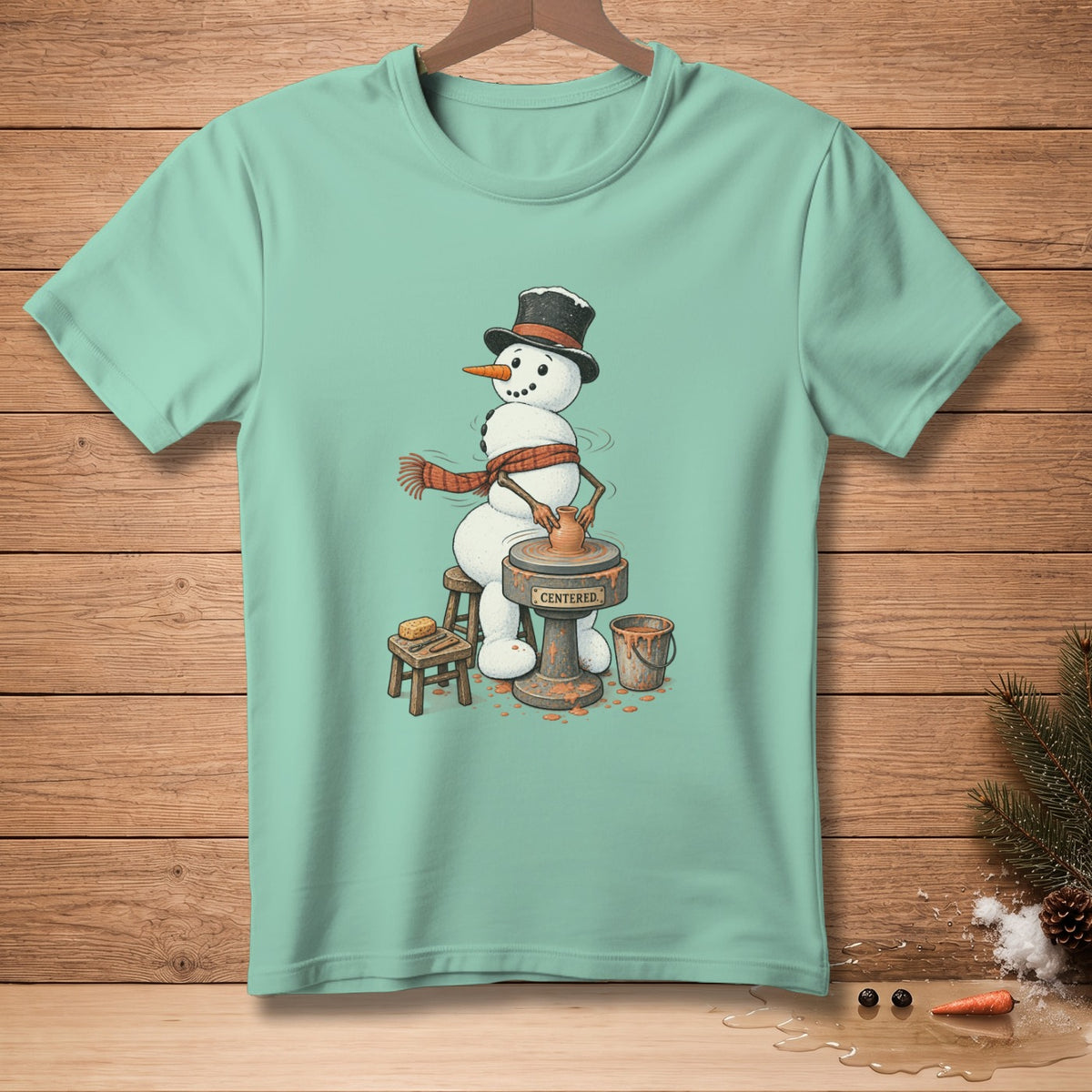 Snowman on pottery wheel with text "CENTERED." on mint green t-shirt.