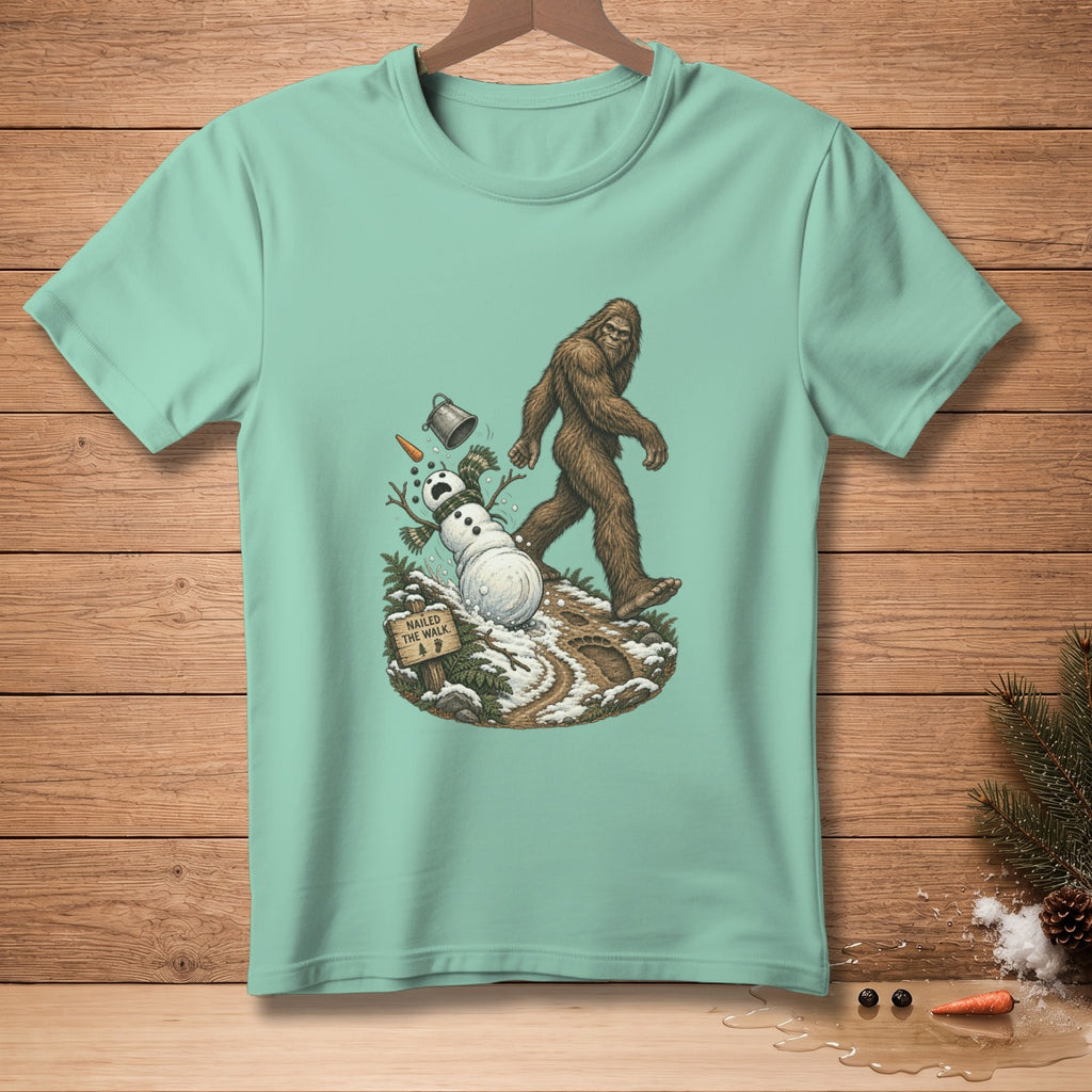 Bigfoot walks by a fallen snowman with a "Nailed the Walk" sign.