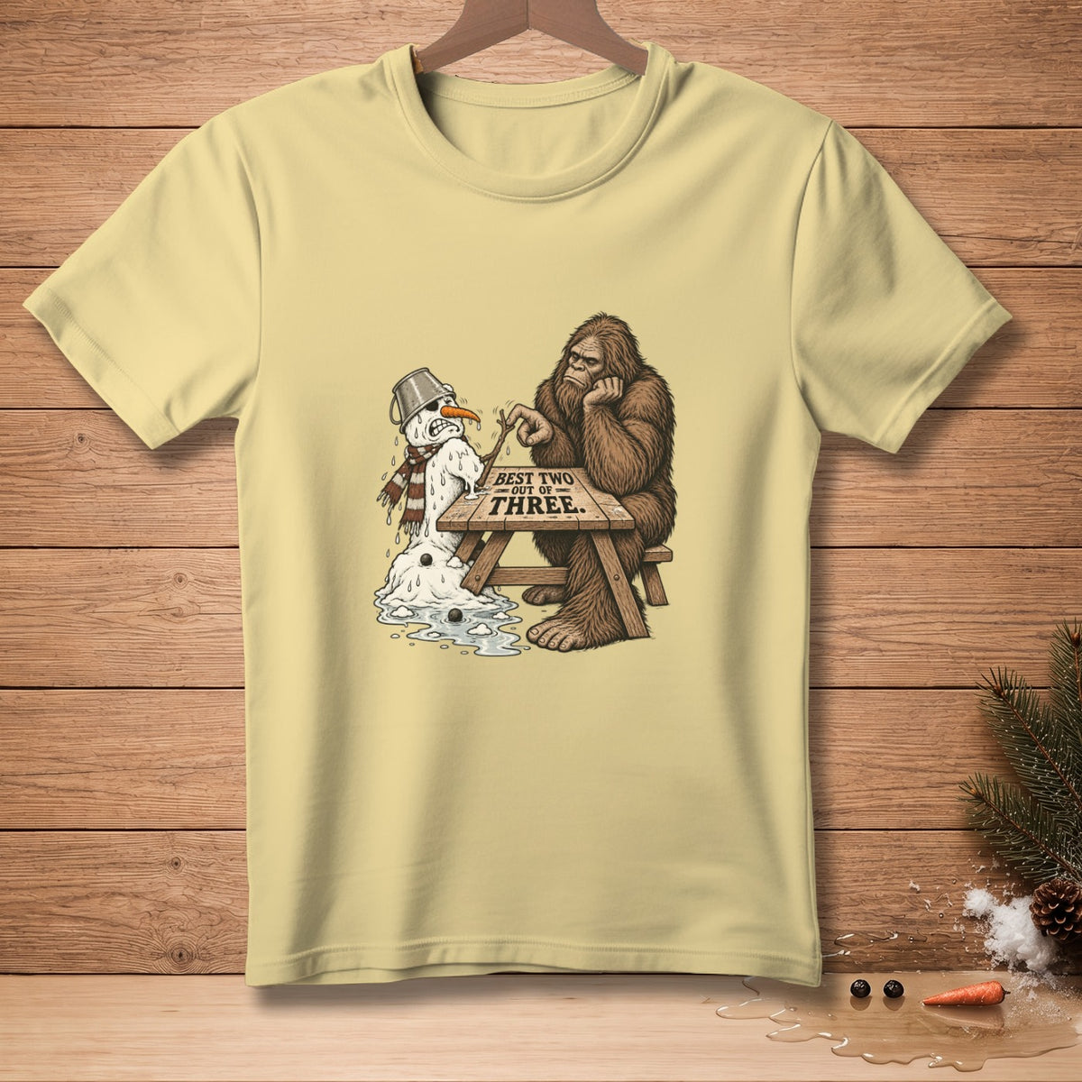Bigfoot sits at a picnic table with a melting snowman, text reads "BEST TWO OUT OF THREE."