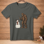 Bigfoot holding stick by snowman wearing hat and scarf on dark grey t-shirt.
