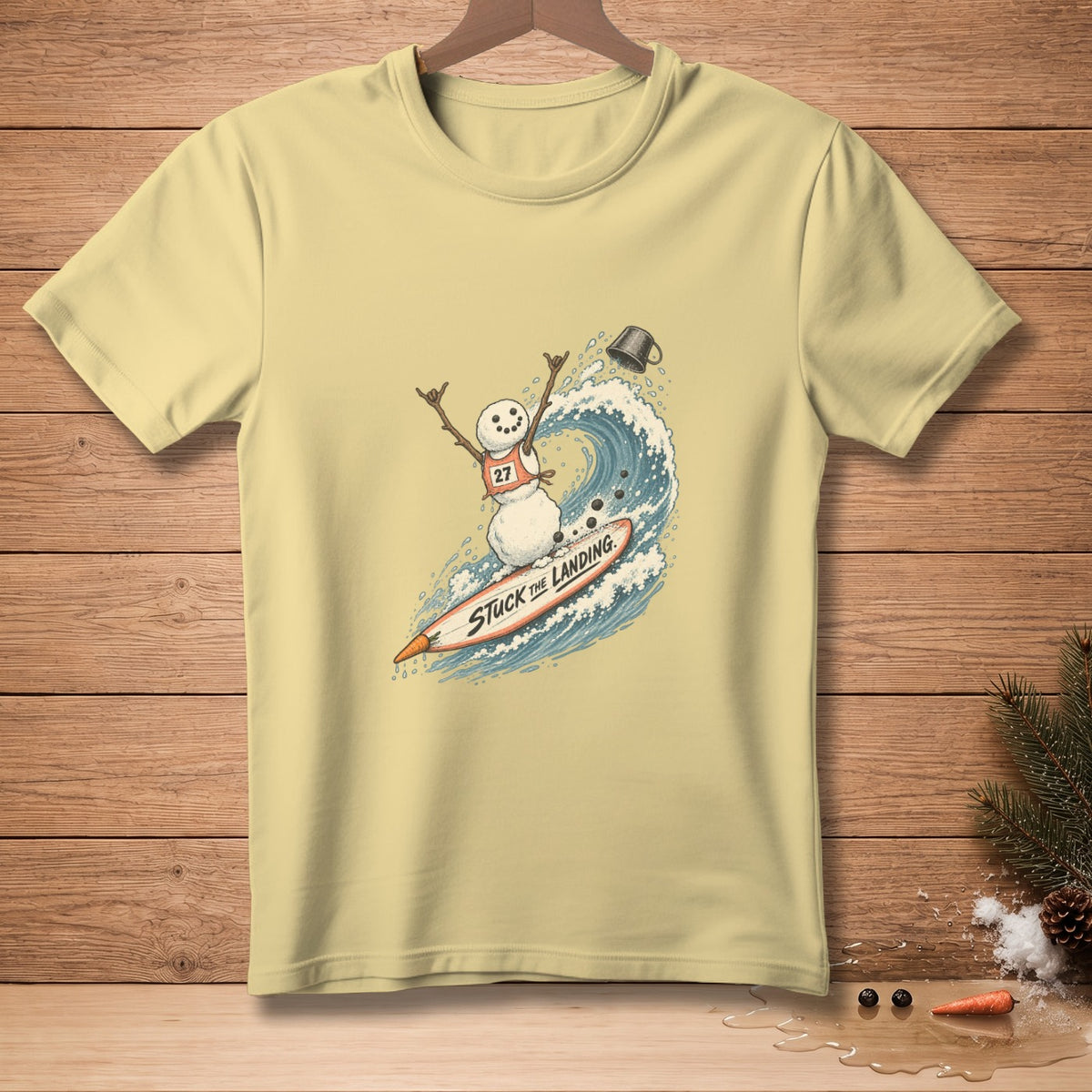 Pale yellow t-shirt with a graphic of a snowman surfing a wave.
