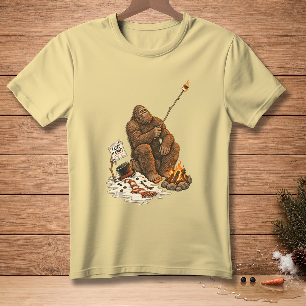 Bigfoot roasts a marshmallow over a campfire, with a melting snowman and "I like it crispy" sign.