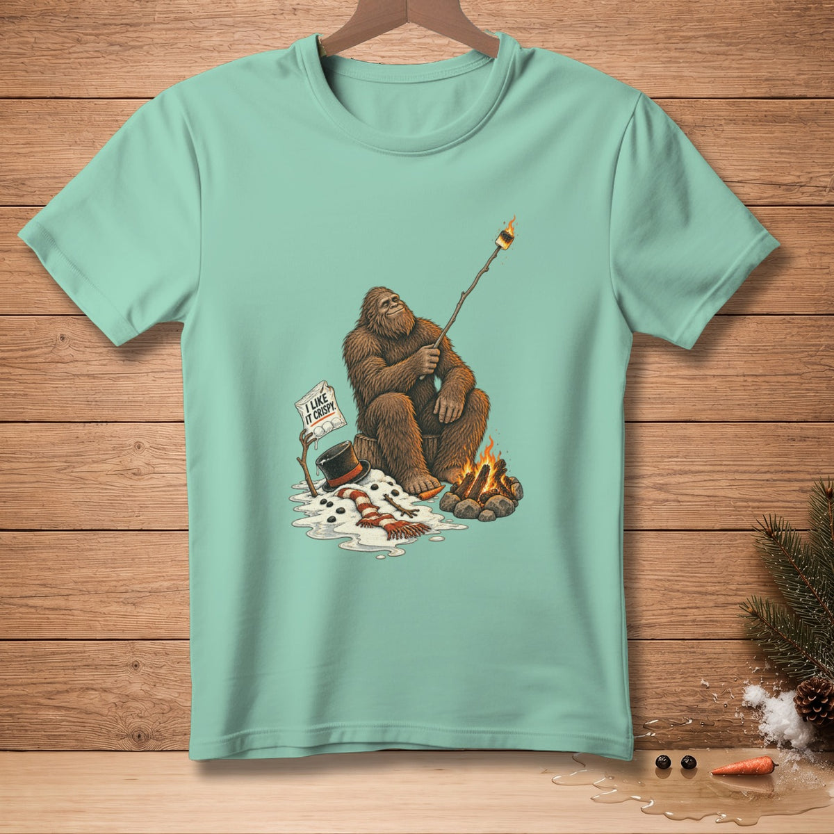 Bigfoot roasts a marshmallow over a campfire next to a melting snowman, text reads "I like it crispy."