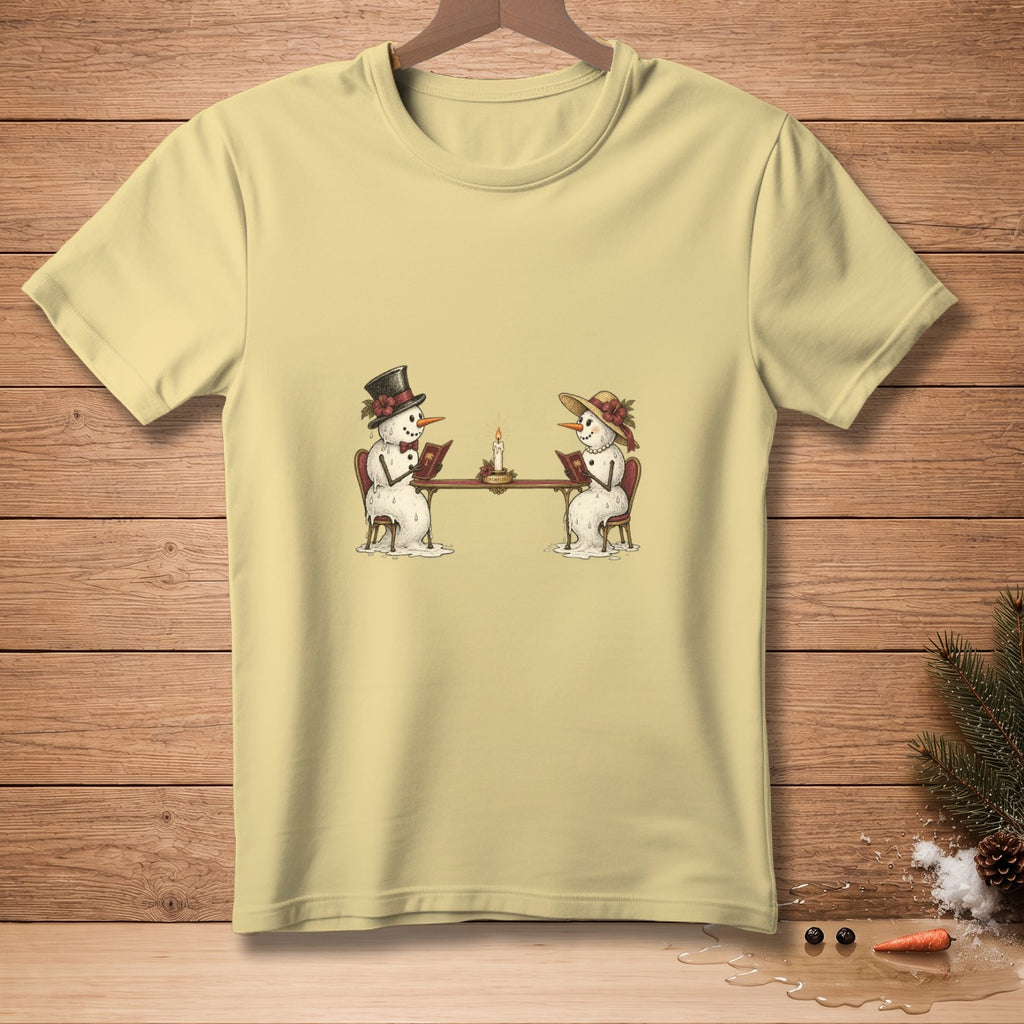 Snowmen reading at a table with a candle, on a pale yellow t-shirt.