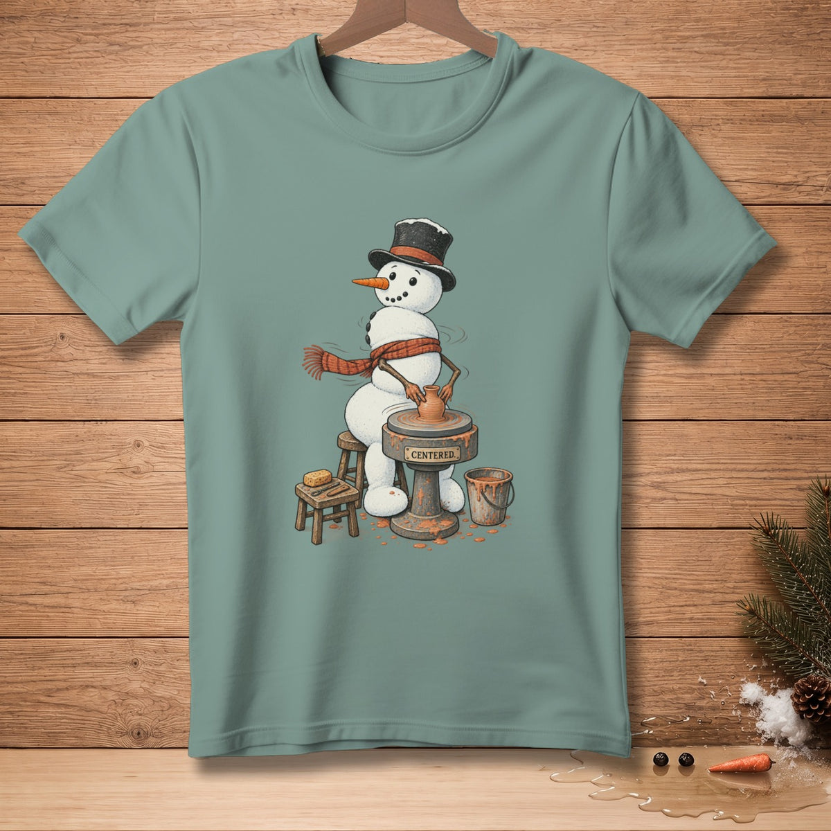 Snowman wearing a hat and scarf, making pottery on a wheel with the word "CENTERED" on it.