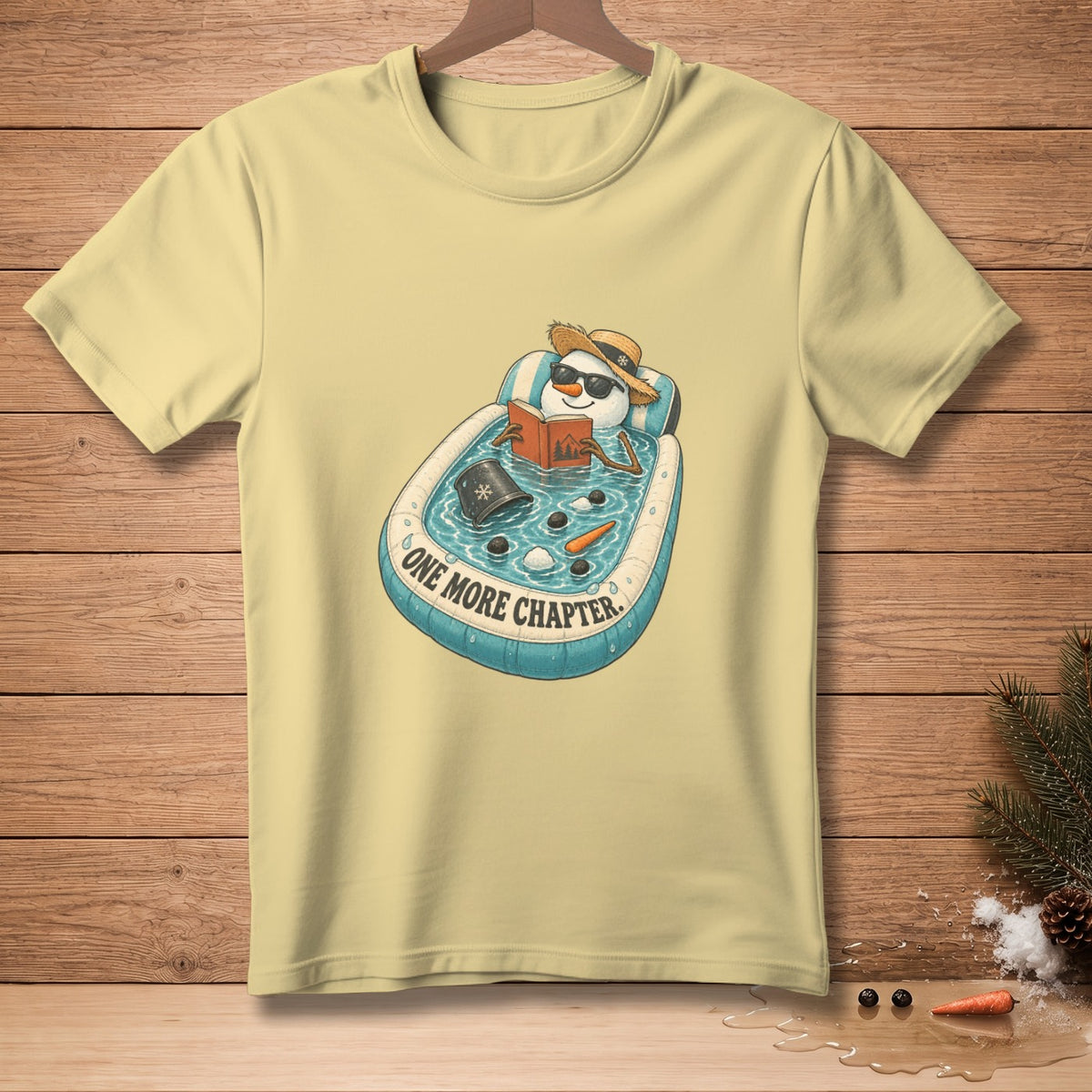 Light yellow t-shirt with a snowman reading in an inflatable pool with text "One More Chapter".