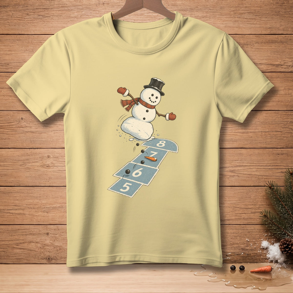 Light yellow t-shirt with a snowman playing hopscotch, wearing a top hat and scarf.