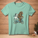 Bigfoot rides a tandem bicycle with a melting snowman that says "I'M HELPING."