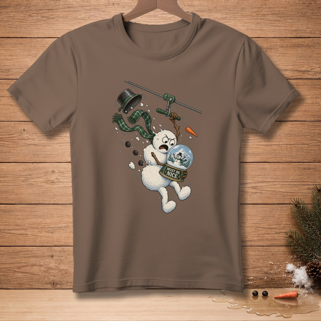 Brown t-shirt featuring a cartoon snowman ziplining with a snow globe and "Must Be Nice" sign.