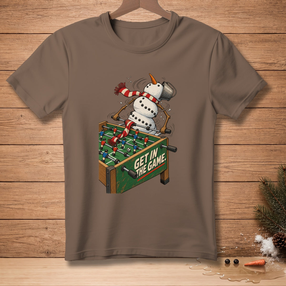 Snowman playing foosball with text "GET IN THE GAME" on a brown t-shirt.