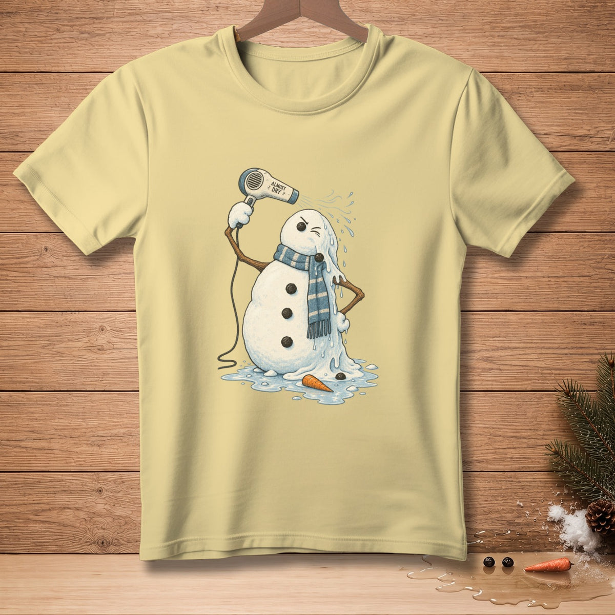 Light yellow t-shirt with melting snowman using a hairdryer, text reads "ALMOST DRY".