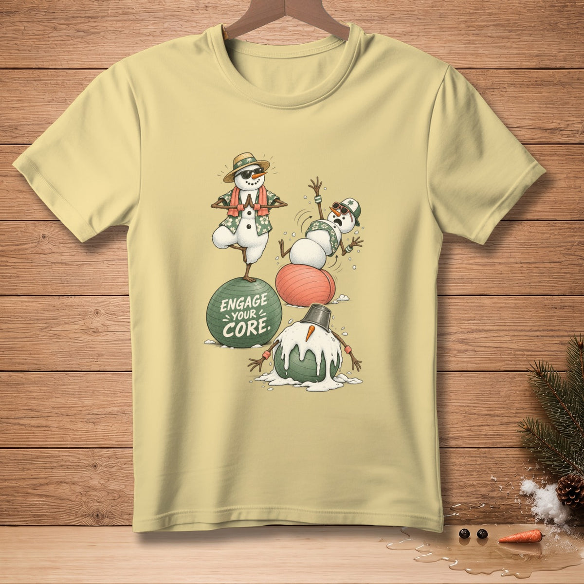 T-shirt graphic of snowmen exercising, one on a green ball with text "ENGAGE YOUR CORE".