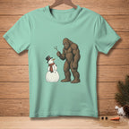 Bigfoot holds a stick, looking at a snowman wearing a hat and scarf.