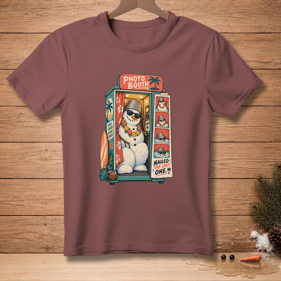 T-shirt graphic: snowman in a photo booth with sunglasses and leis, "Nailed the last one" text.
