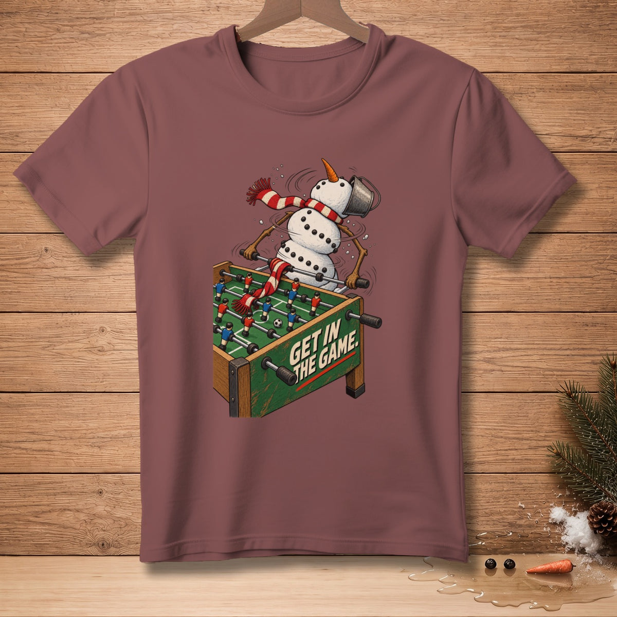 Snowman playing foosball with text "GET IN THE GAME" on a burgundy t-shirt.
