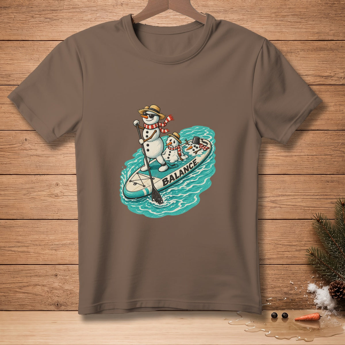 Snowmen on a paddleboard with "BALANCE" text, on a brown t-shirt.