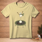 Pale yellow t-shirt with a jumping snowman illustration on a trampoline.