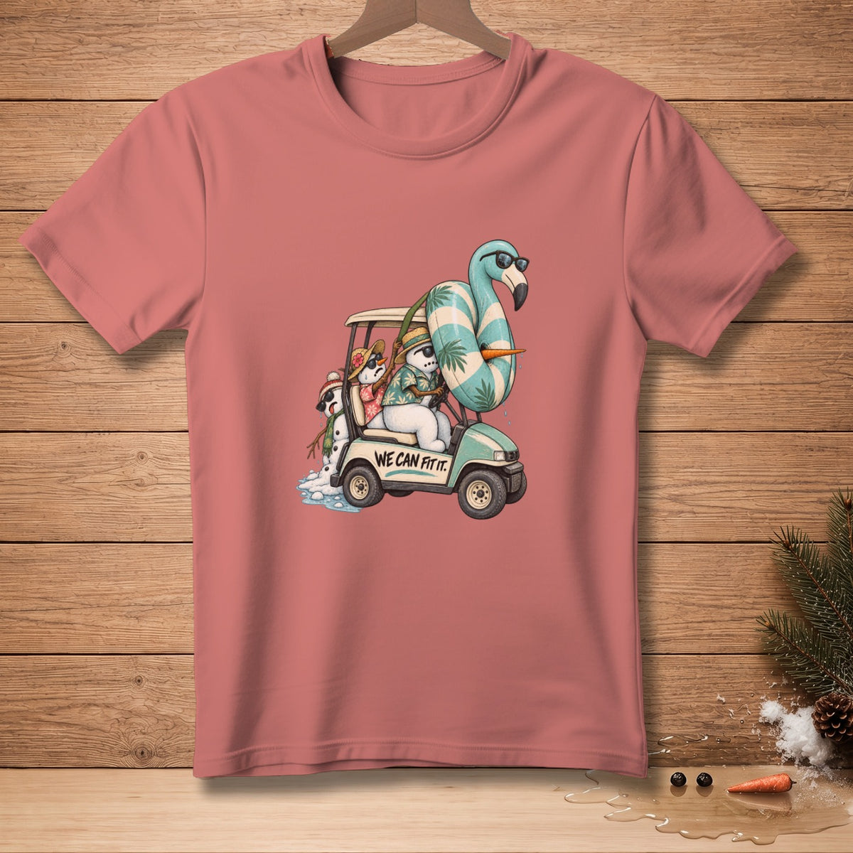 T-shirt with a graphic of snowmen in a golf cart with a flamingo float and the text "WE CAN FIT IT."