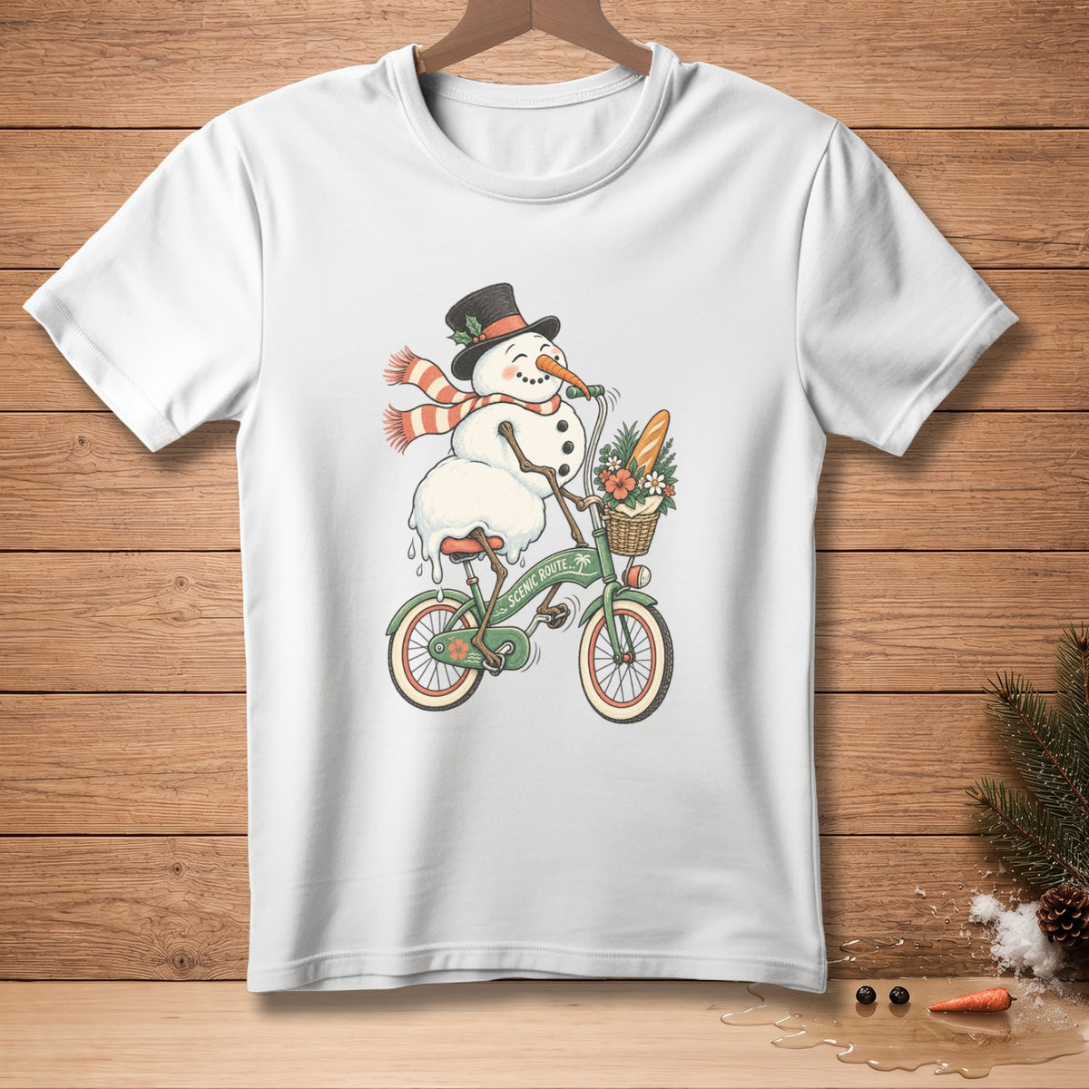 White t-shirt with a snowman wearing a hat and scarf riding a bicycle with a basket.