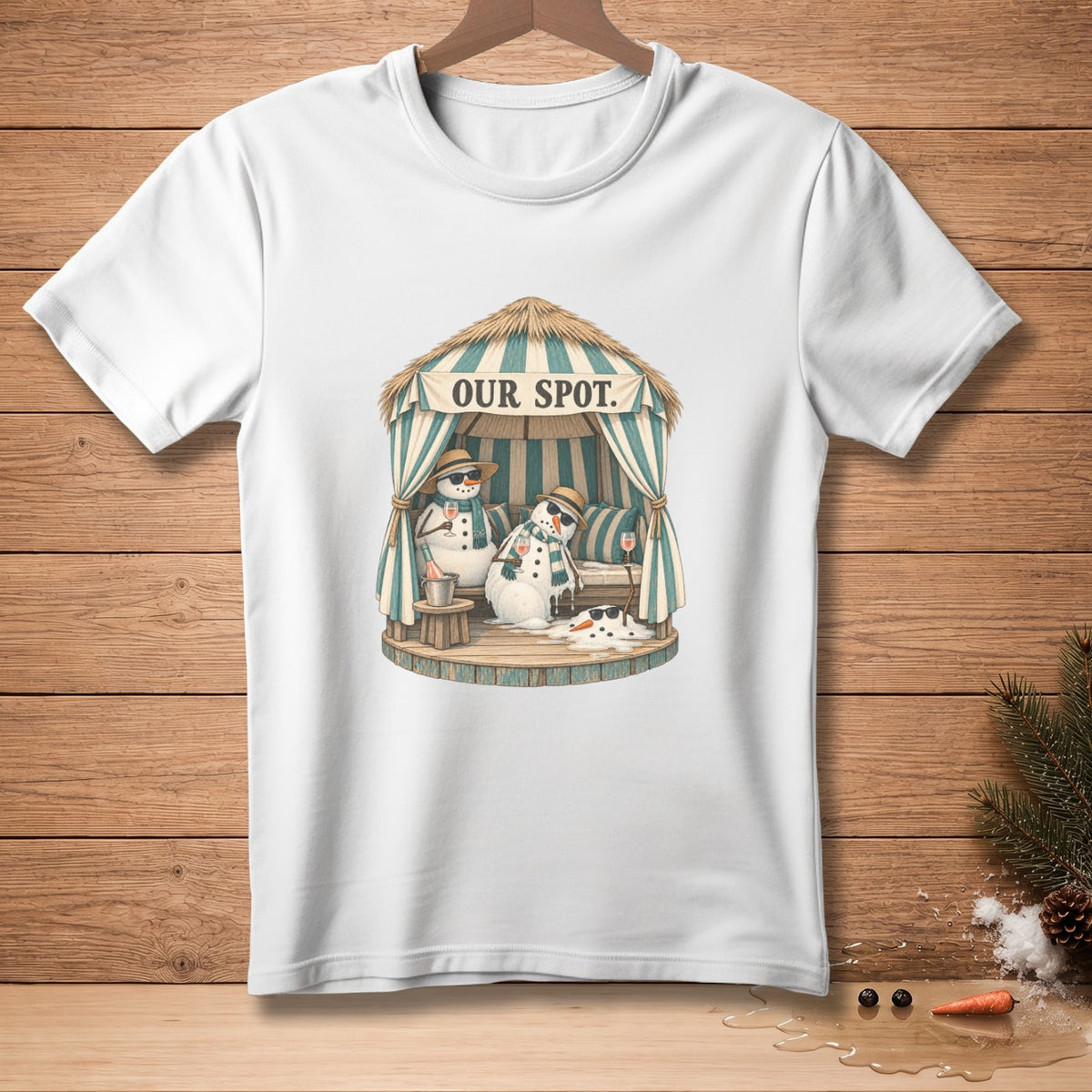 White t-shirt with a graphic of snowmen relaxing under a thatched cabana labeled "OUR SPOT."