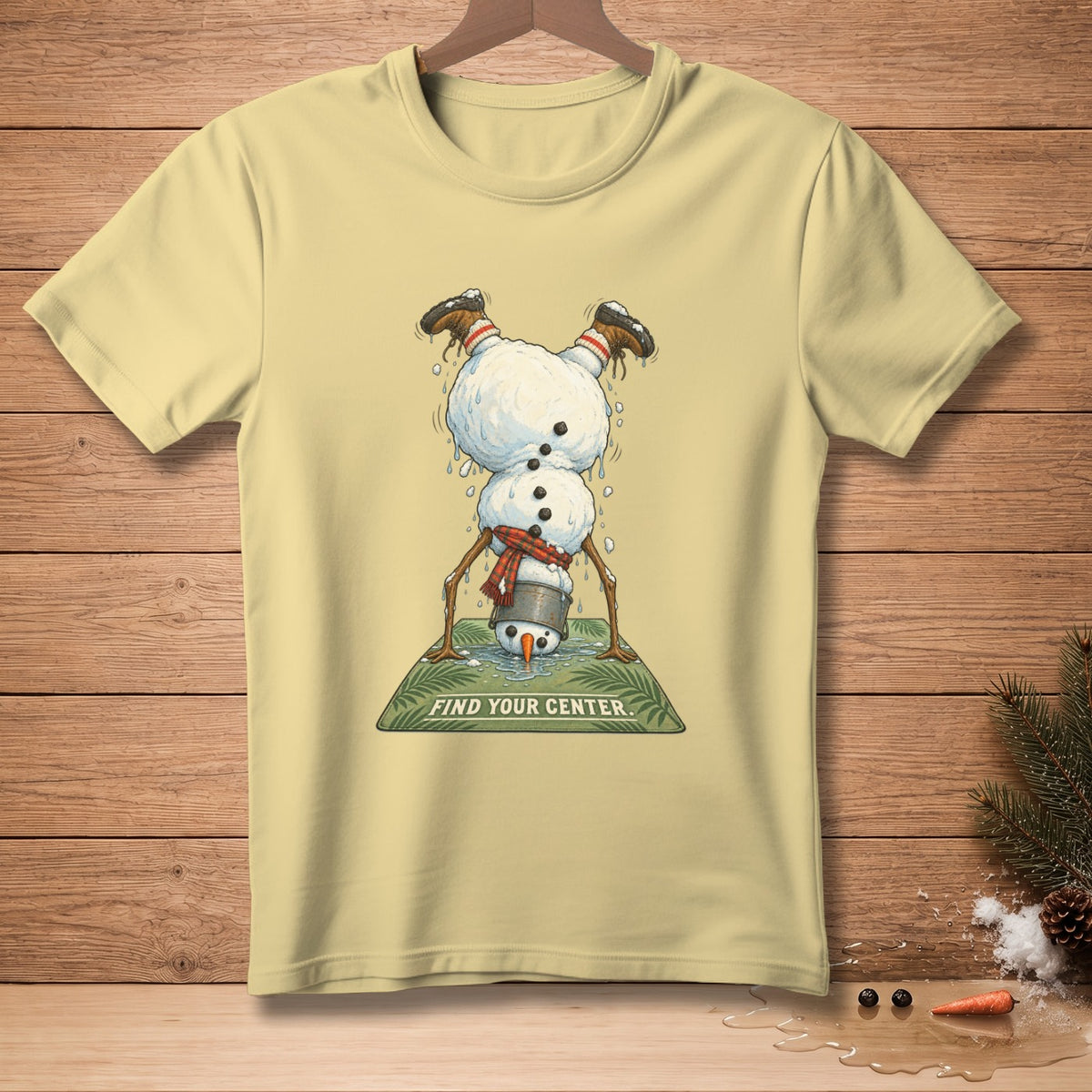 Light yellow t-shirt featuring a melting snowman doing a handstand on a green mat that says "FIND YOUR CENTER."