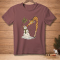 Giraffe feeding a melting snowman a carrot on a maroon t-shirt.