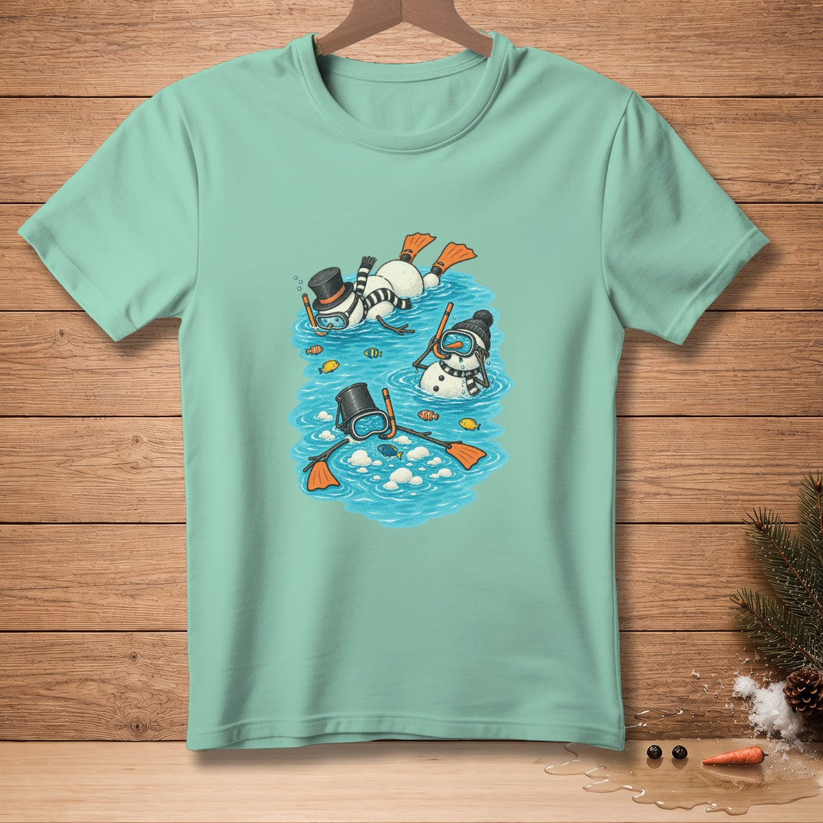 Three snowmen in snorkel gear swim with fish in blue water on a light teal shirt.