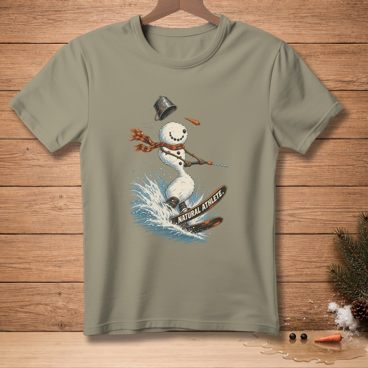 Snowman waterskiing with text "NATURAL ATHLETE" on a light brown t-shirt.