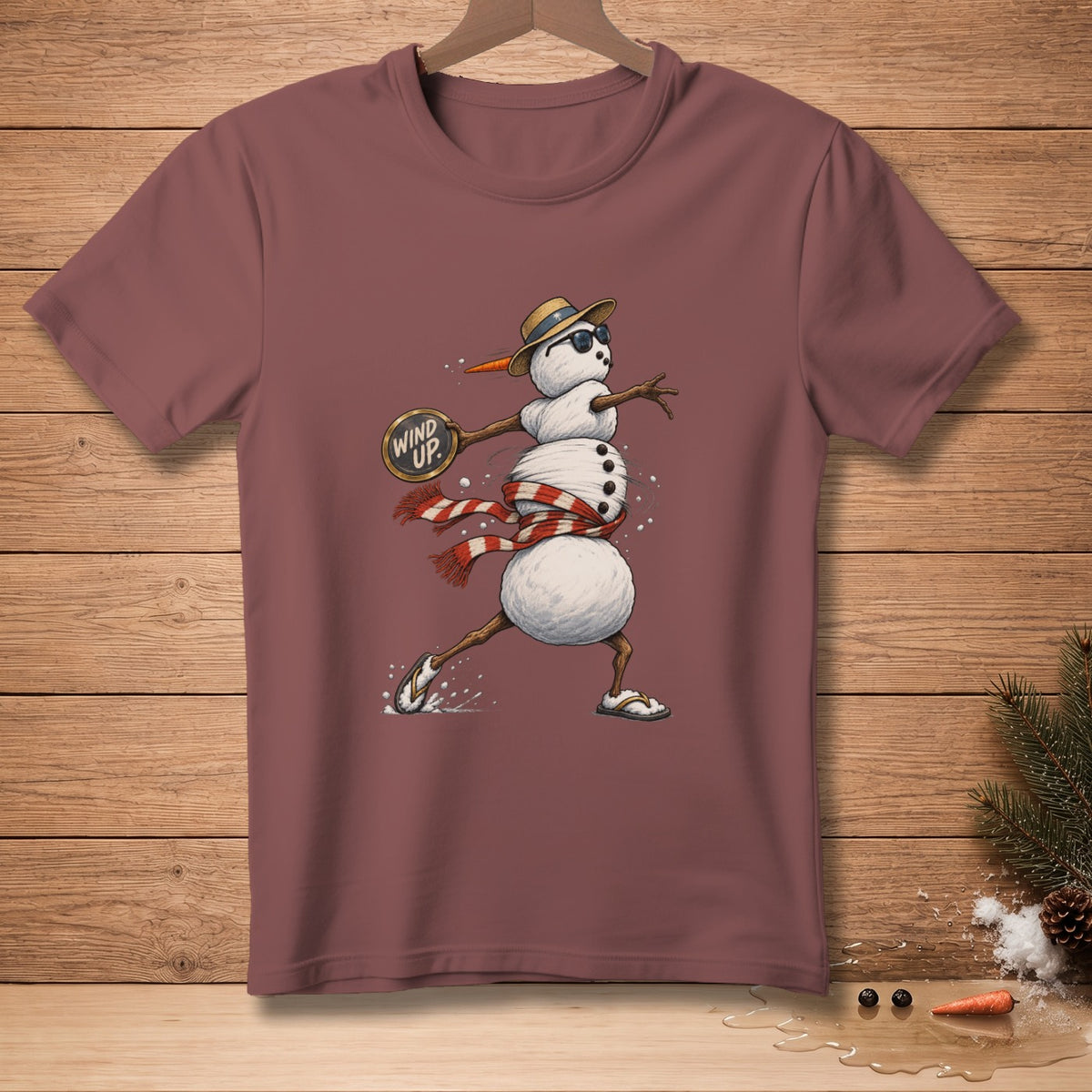 Maroon t-shirt with a cartoon snowman wearing a hat, sunglasses, and scarf, holding a sign.