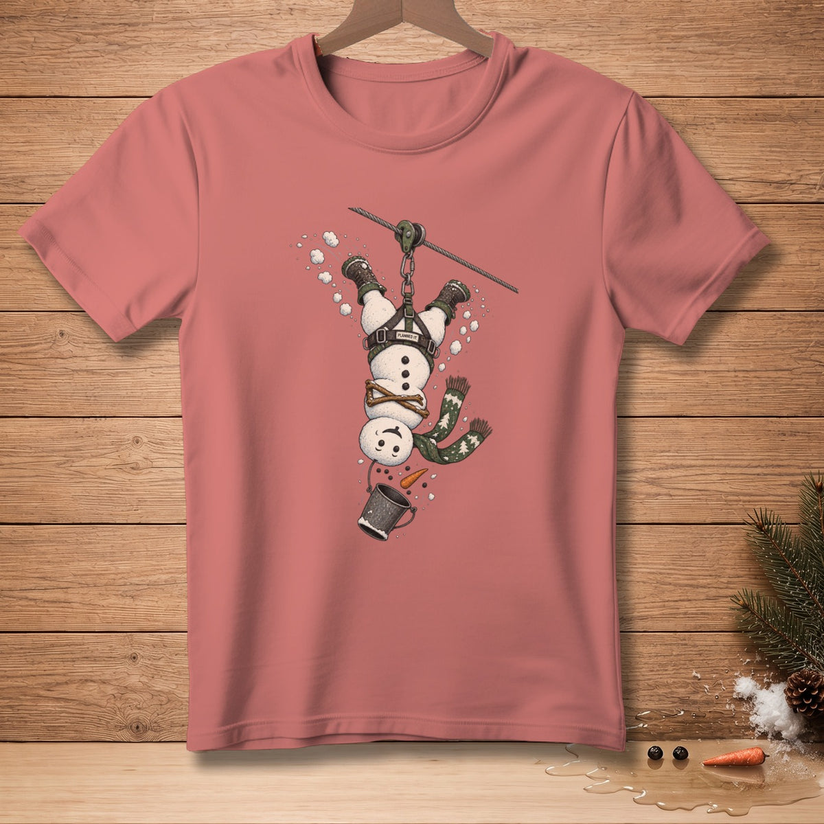 Pink t-shirt with a graphic of a snowman ziplining upside down.
