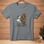 Bigfoot rides a bicycle with a melting snowman, text says "I'M HELPING".