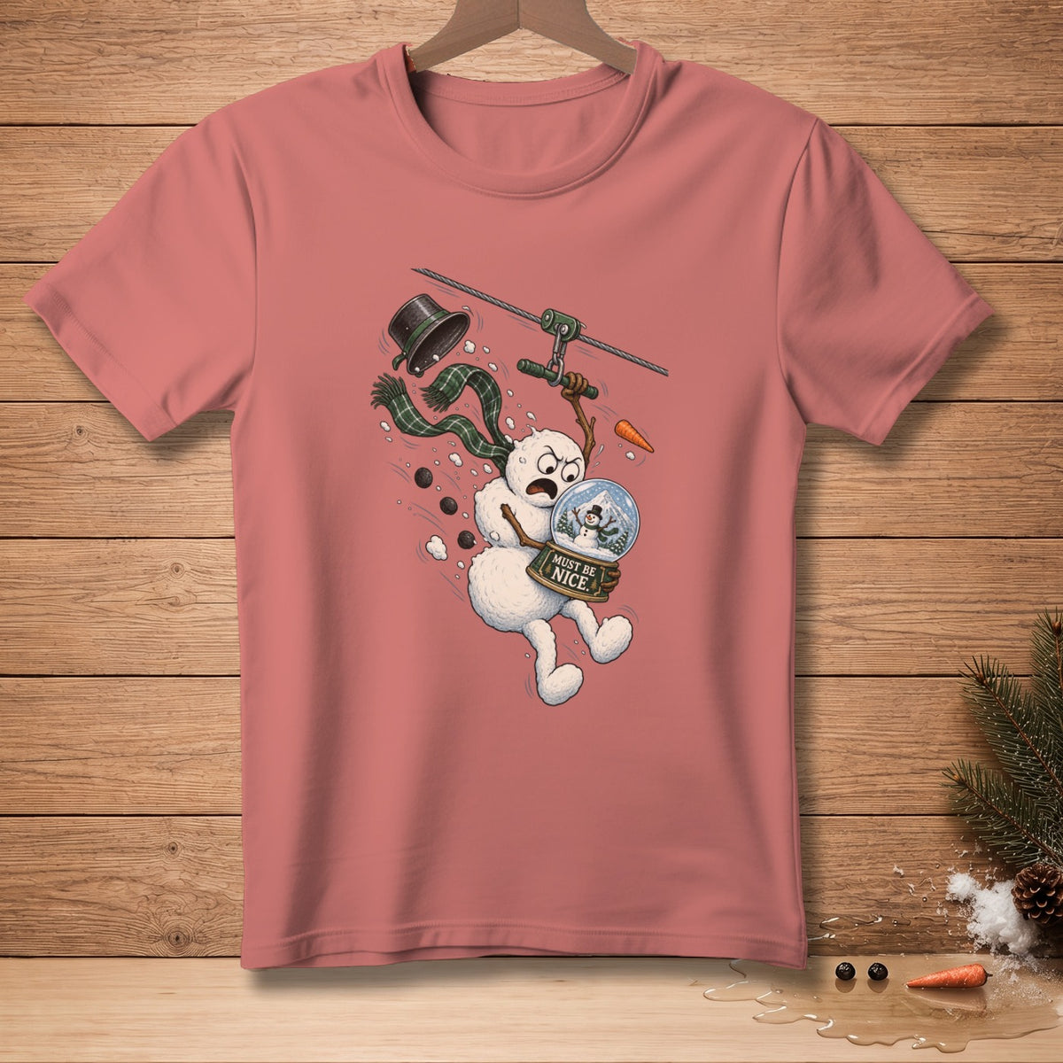 Pink t-shirt with illustration of a panicked snowman ziplining with a snow globe.