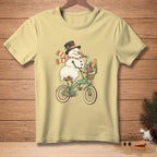 Snowman wearing a hat and scarf rides a bicycle with a basket of flowers and bread.