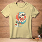 Pale yellow t-shirt with melting snowman holding a ball that says "ALMOST THERE."