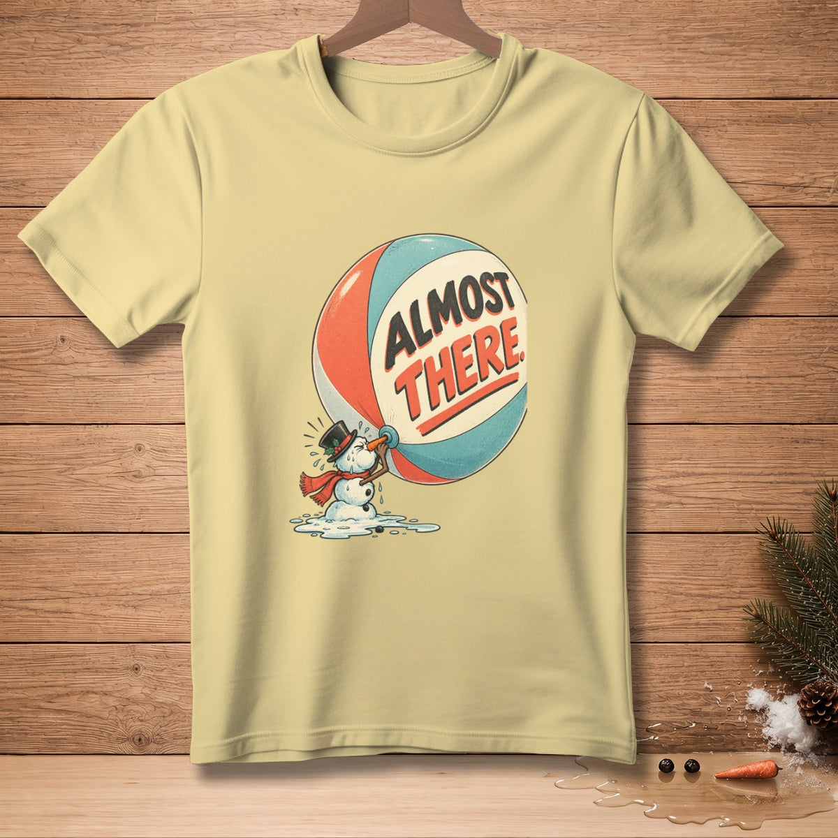 Pale yellow t-shirt with melting snowman holding a ball that says "ALMOST THERE."