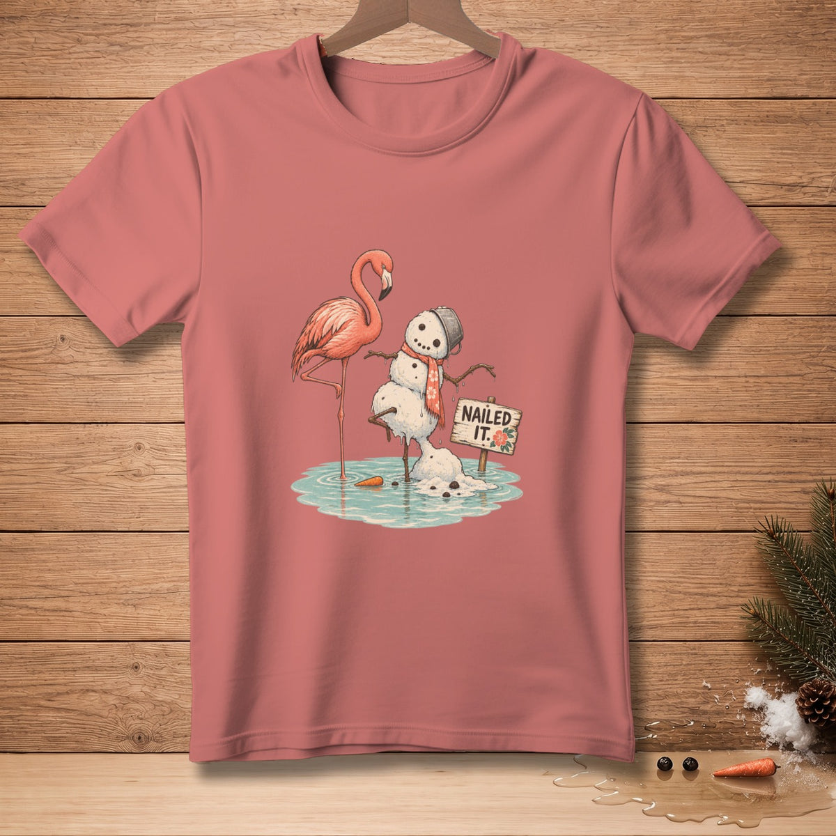 Pink t-shirt with a flamingo and melting snowman graphic that reads "Nailed It."