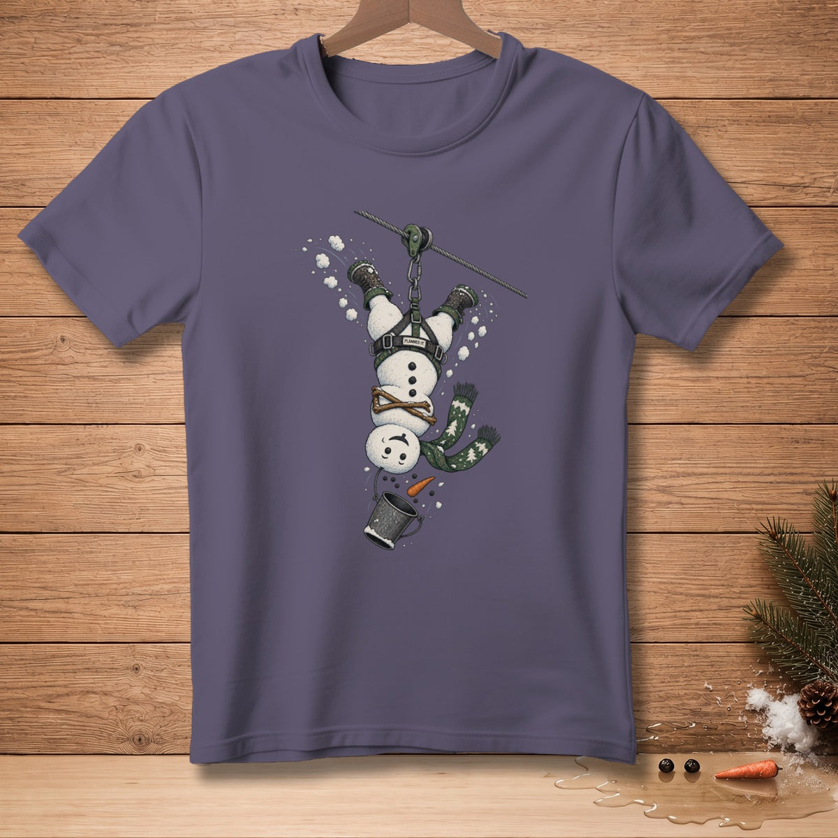 T-shirt with a cartoon snowman zip-lining upside down, wearing a harness.