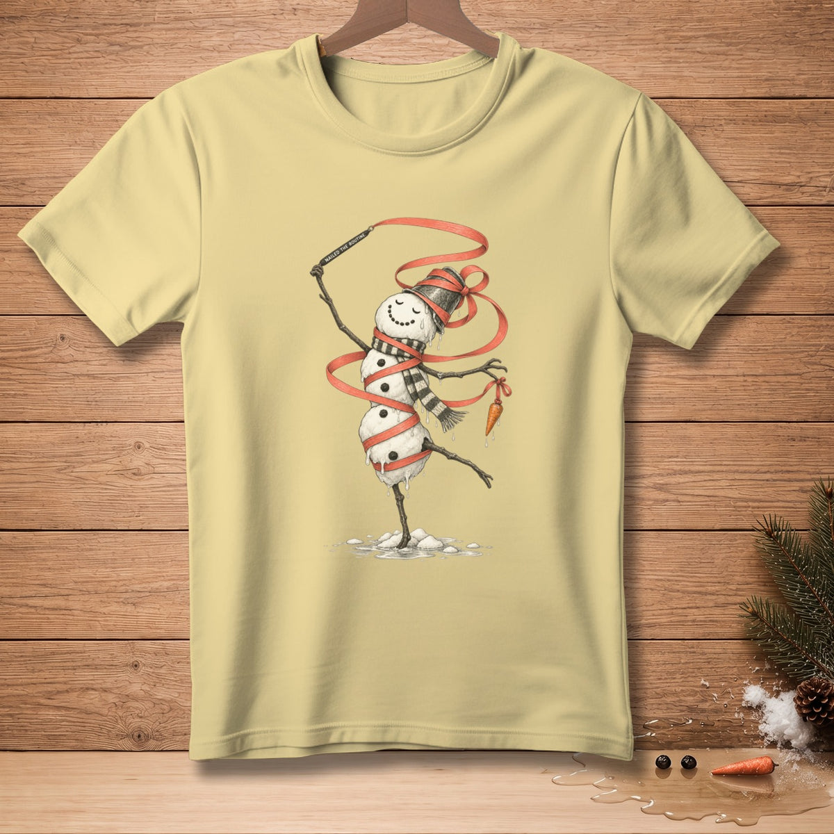 Light yellow t-shirt featuring a cartoon snowman dancing with a red ribbon and holding a carrot.